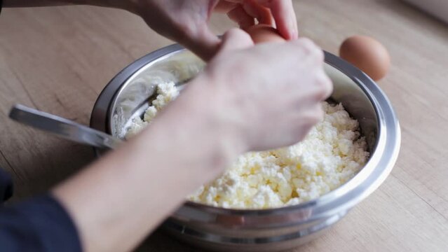 Dip the egg into the flour with cottage cheese and stir for the cheesecake. Female hands prepare white cottage cheese for cooking in a metal bowl in the kitchen.