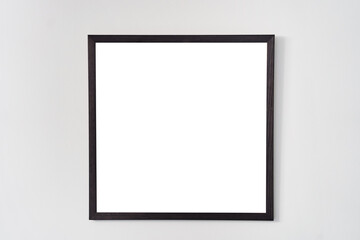 An empty square photo frame with a black border hanging on a white wall. High quality photo