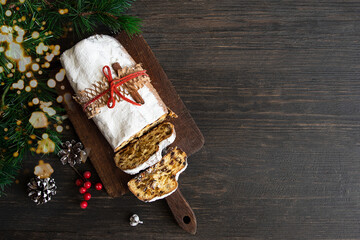 Top view of German fruit bread Stollen on cut board with Christmas decoration on wooden background with copy space