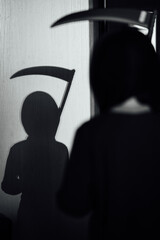 The shadow of a child with a scythe dressed as death on Halloween