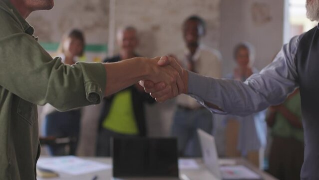 business handshake - people shaking hands after meeting - colleagues in background clapping hands - team welcoming