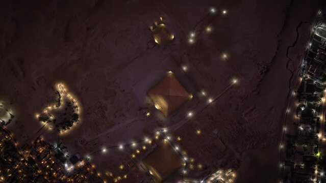 Aerial top view of the Pyramids of Giza at dusk in Egypt. The three pyramids illuminated at night