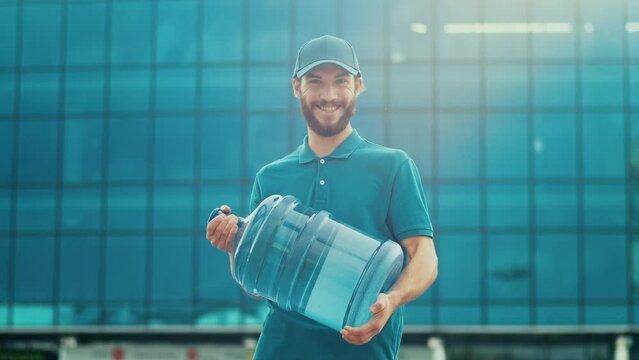 Portrait of Handsome Delivery Person in Uniform Holds a Big Bottle of Water and Smiles. Courier Working in Logistics Distribution Center, Delivering Online Orders. Great delivery service.
