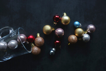 Glass with colorful Christmas baubles on dark background. Top view.