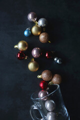 Glass with colorful Christmas baubles on dark background. Top view.