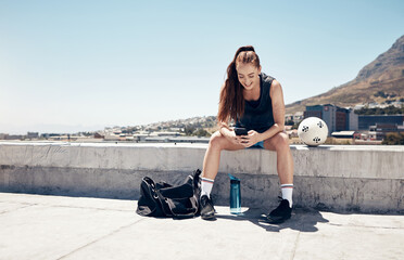 Sports woman, phone and football or soccer workout on city building rooftop for break or rest with...