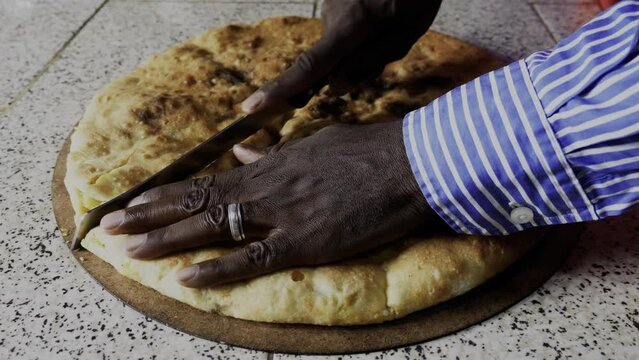 A traditional Moroccan Berber pizza is being cut into pieces. Authentic, a local dish served in Erfoud, Rissani, and Erfoud, South Morocco. Pizza filled with vegetables, meat, eggs, and herbs.