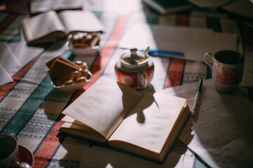 Books and papers are scattered on the table among the tea dishes. Work mess. Evening or morning light falls on the still life.