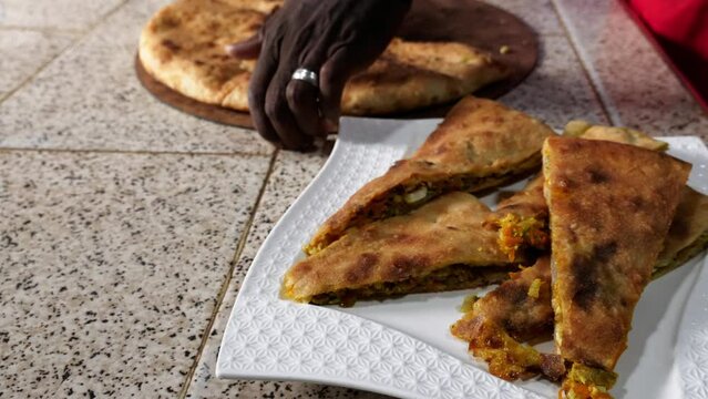 A traditional Moroccan Berber pizza is being cut into pieces. Authentic, a local dish served in Erfoud, Rissani, and Erfoud, South Morocco. Pizza filled with vegetables, meat, eggs, and herbs. 