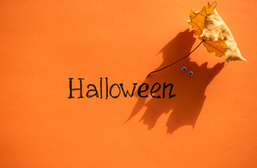 Halloween idea. The inscription Halloween on an orange background next to the shadow from an oak leaf in the form of a ghost with eyes. Festive background.