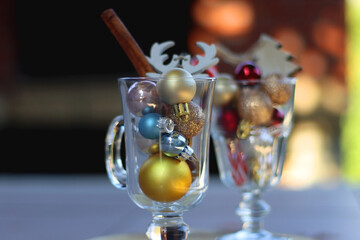Two glass goblets with colorful Christmas ornaments on the table. Selective focus.