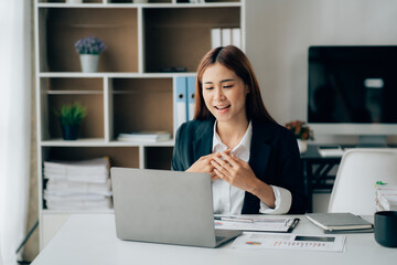 Beautiful Asian woman sitting in the office using a laptop .Happy business woman smiling and enjoying work.