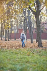 A girl in a knitted sweater in an autumn park runs along the path. September or October, yellow leaves on trees.
