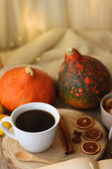 Cup of tea or coffee, seasonal spices, bowl of cookies, blanket, pumpkins, colorful leaves, books and tangerines on wooden table. Cozy hygge at home. Selective focus.