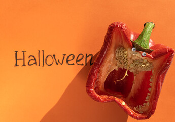 Idea for Halloween. Red pepper with eyes depicts a monster with an open mouth on an orange background next to the inscription Halloween. Sinister monster.