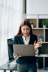 Happy young asian businesswoman sitting on her workplace in the office. Young woman working at laptop in the office