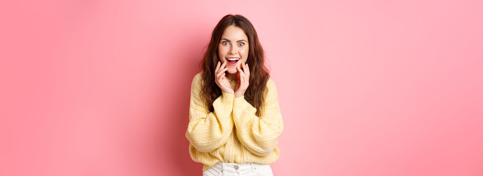 Omg Really. Excited Young Woman Hear Gossip Or Super Good News, Staring Amazed, Smiling And Holding Hands On Face, Listen To Interesting Rumor, Standing Over Pink Background