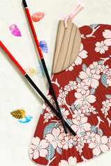 Obraz premium Vertical flat lay still life with colourful asian chopsticks and fan set against craft paper with metallic leaves 