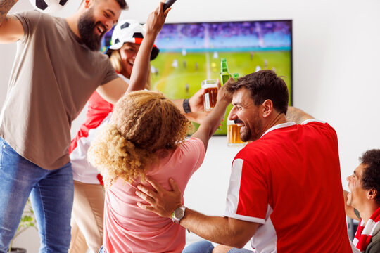 Friends cheering, making a toast and drinking beer while watching football on TV