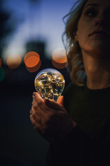 young worried female human holding bright shining lightbulb in her hands feeling unsave while...