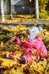 baby little girl sitting on the ground on yellow leaves in autumn