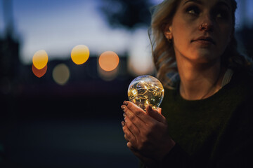 young worried female human holding bright shining lightbulb in her hands feeling unsave while...