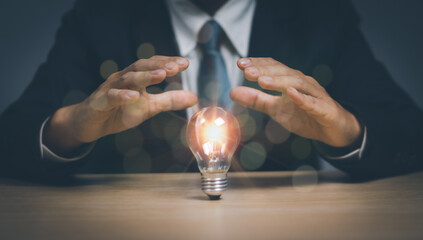 Businessman showing power of protection with light bulb on wooden table, concept of creative ,...