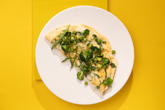amlet with egg and greens on a white plate on a yellow background