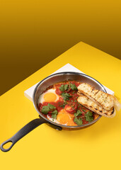 amlet with tomato and toast in a frying pan on a yellow background