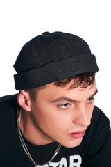 Cropped close-up shot of a young man in a black docker cap with a turn up brim. A guy in a black T-shirt and a denim cap without a visor is posing on a white background. Side view.