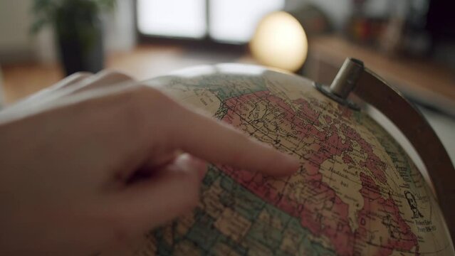 White hand stopping a globe from spinning and pointing to Canada.