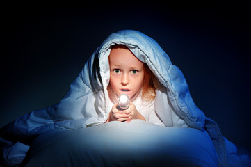 Little girl hiding under the blanket with a flashlight - obrazy, fototapety, plakaty