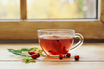 A glass cup of rosehip tea with fresh berries in a glass cup on a wooden windowsill. Vintage background, selective focus