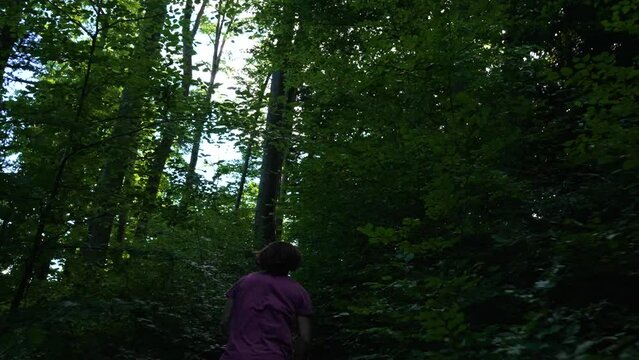Young man with red tshirt is running up a small path in a dark forest in slow motion. camera is following him, first person view modus.