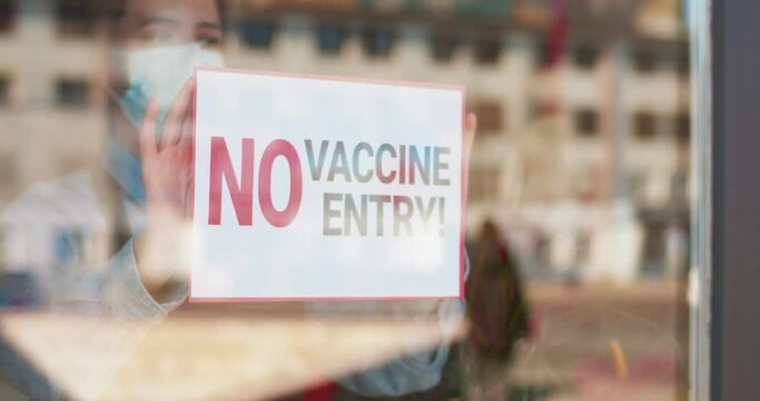 Only for vaccinated. Descrimination. Vax. Vaccination. Covid-19. Close up of womans hands attaching sign on the glass in pandemic time. Pandemic of coronavirus.