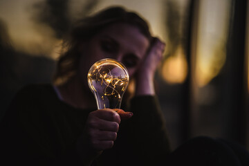 young worried female human holding bright shining lightbulb in her hands feeling unsave while...