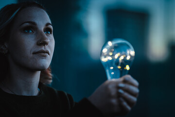 young worried woman holding bright shining lightbulb in her hands feeling unsave while in fear...
