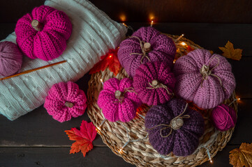 pink colored crochet pumpkins with autumn leaves on dark brown wooden ground with crochet hook and woolen balls