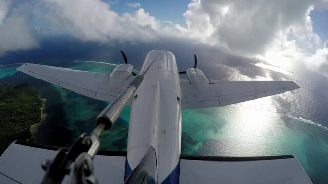 External perspective of twin engine plane flying over coastline, reef and ocean