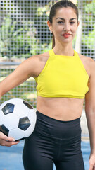 Young latin woman looking at camera and smiling with a soccer ball in her hands.