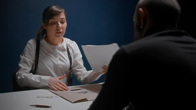 Female detective cop interrogates suspected criminal in handcuffs. Police officer opens dossier folder with documents. FBI agent asks to sign papers. Detained mafia refuses to sign without his lawyer