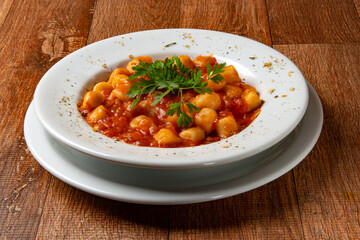Gnocchi dish with tomato sauce and parsley on rustic wooden table.