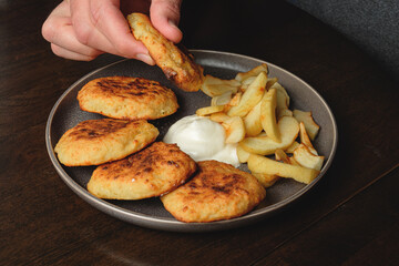 A man eats curd fritters with his hands .Cottage cheese pancakes,curd fritters with fresh apple slices  and sour cream in a dish. Gourmet Breakfast
