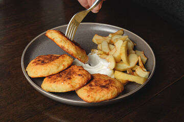 А man eats curd fritters with a fork. Cottage cheese pancakes,curd fritters with fresh apple slices  and sour cream in a dish. Gourmet Breakfast
