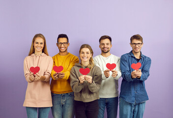 Studio group portrait of happy positive joyful kind smiling mixed race multiethnic young people holding red paper hearts standing isolated on purple color background. Love and Valentine's Day concept