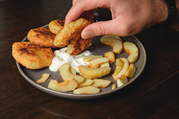 A man eats curd fritters with his hands .Cottage cheese pancakes,curd fritters with fresh apple slices  and sour cream in a dish. Gourmet Breakfast
