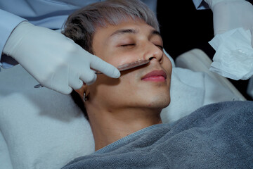 Fototapeta premium Beautician applying hydro gel mask on the young man face, before laser treatment in beauty salon. Close up side view. , Beauty clinic concepts.