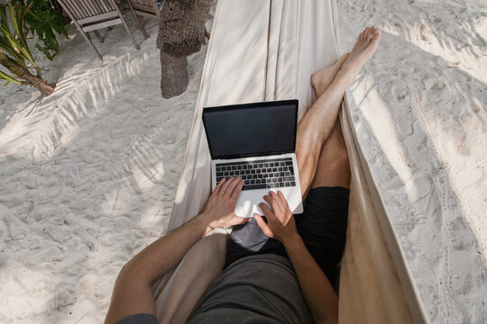 workation, remote work, freelancer with laptop in hammock on tropical beach