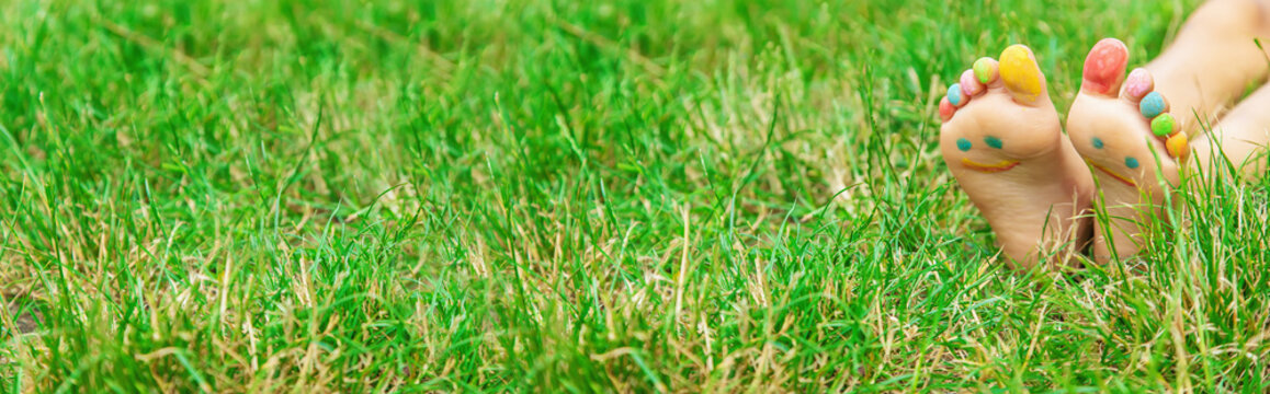 Children's feet with a pattern of paints smile on the green grass. Selective focus.