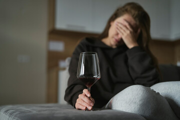 Caucasian woman with alcoholism sitting at the sofa and holding glass of wine